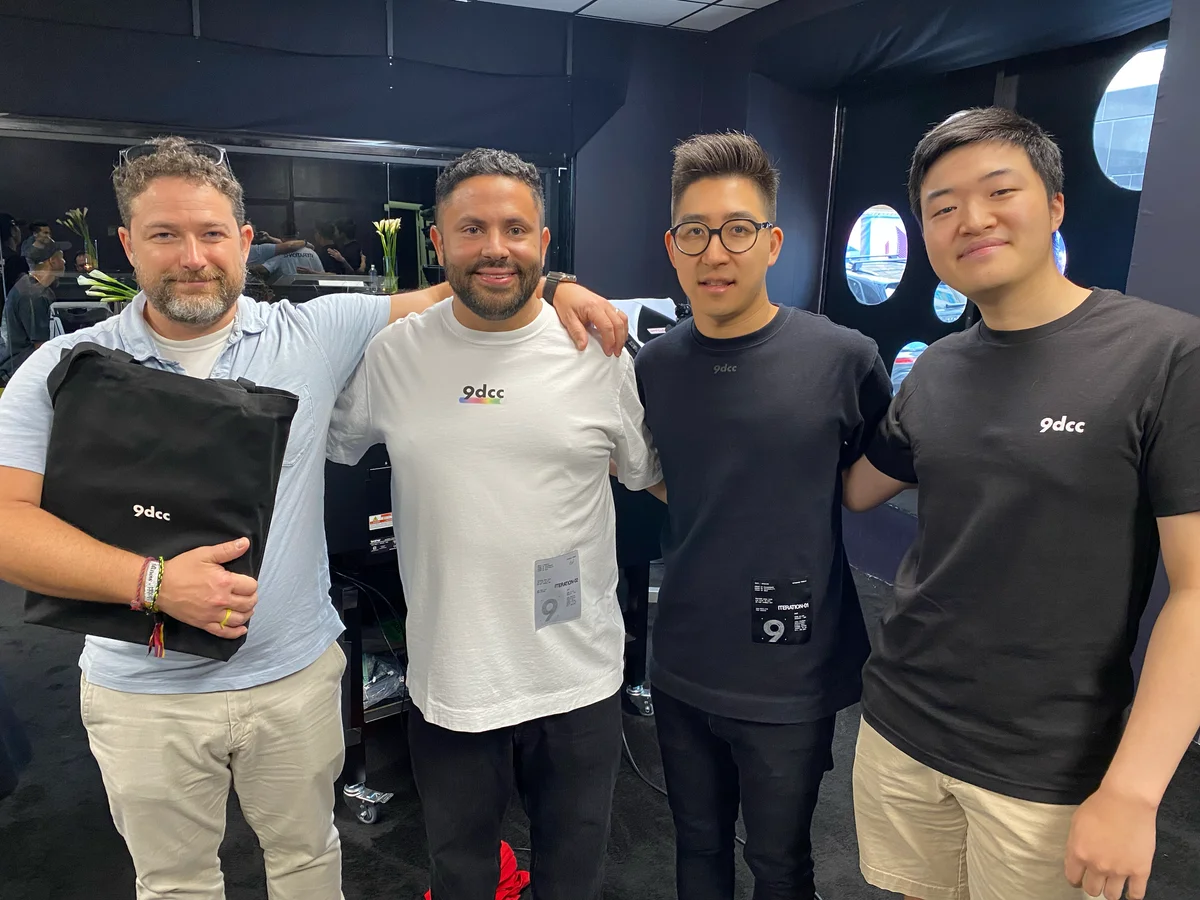 Four people posing together at the 9dcc event, wearing 9dcc shirts and holding a black garment bag.