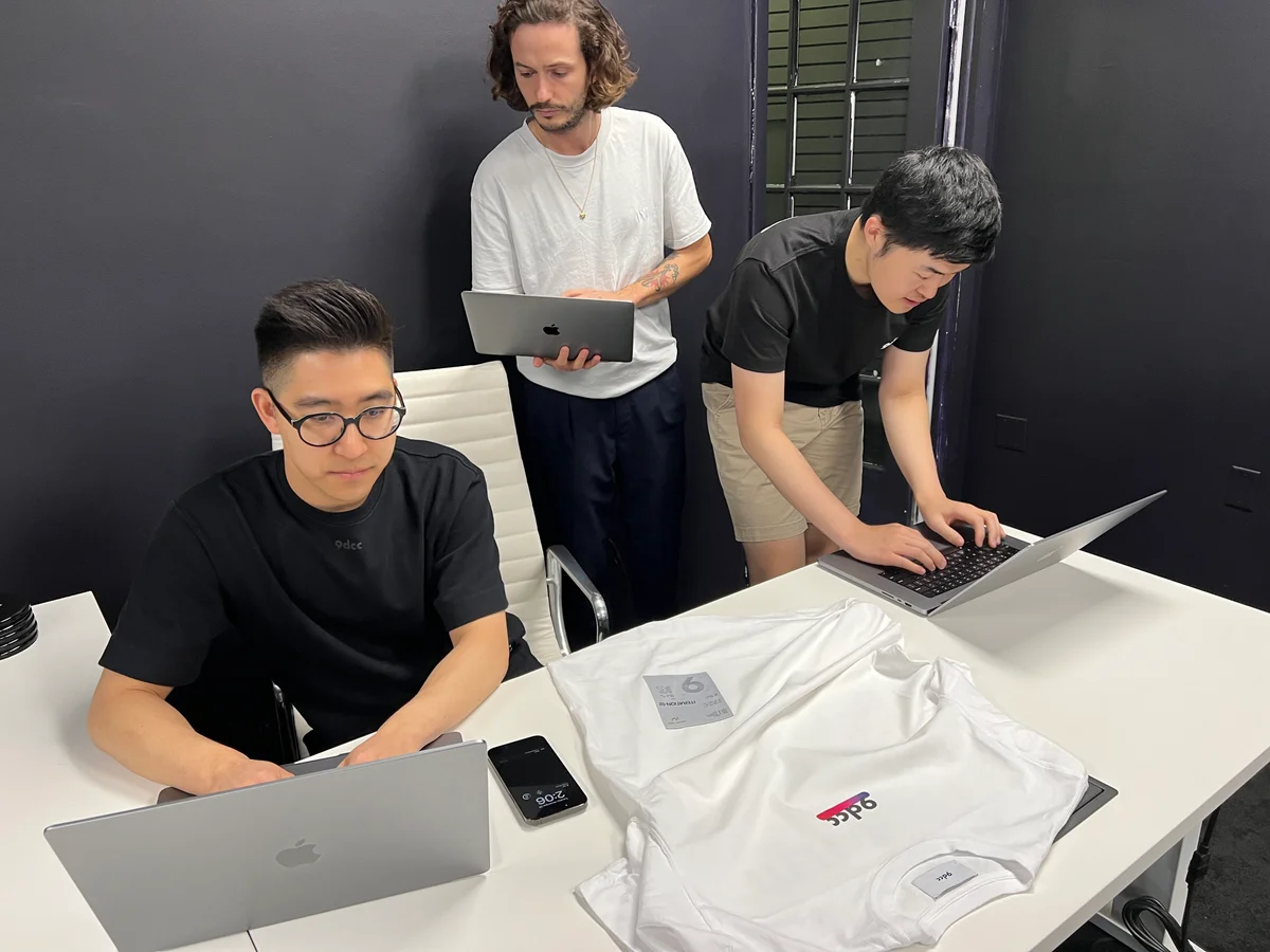 Three people working on laptops around a table with a printed 9dcc shirt laid out in front of them.