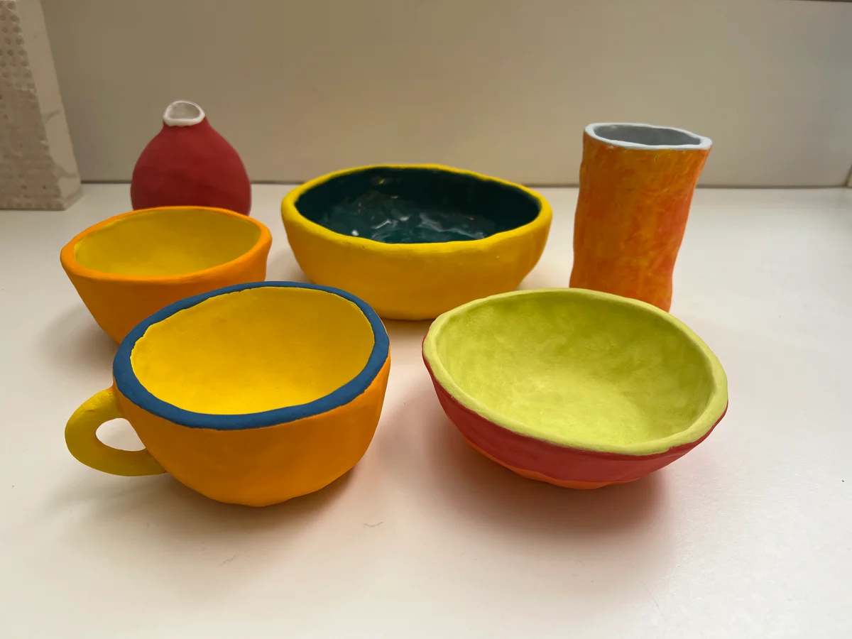 A group of handmade ceramic vessels on a white surface, with yellow, orange, red, green, and blue color combinations.