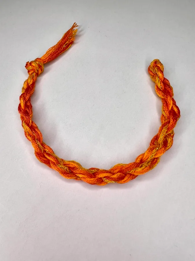 A finished orange-and-gold twisted bracelet with knotted ends on a pale background.