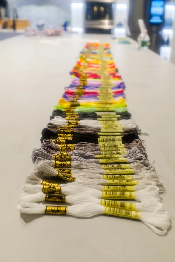DMC embroidery-floss skeins laid out along a white counter, from white and gray in the foreground to bright colors farther back.
