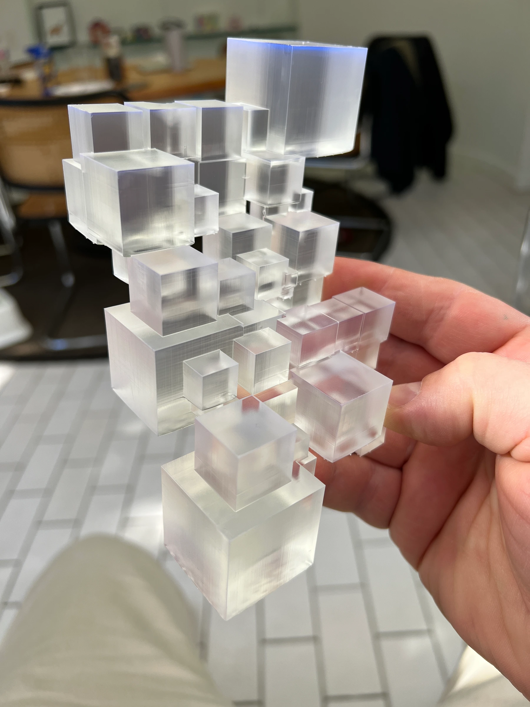 A hand holding a translucent 3D-printed CryptoCube, with the printing layers visible through its stacked cubic forms.