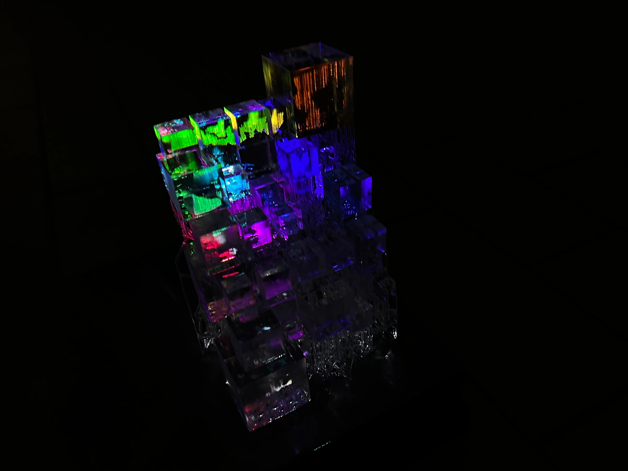 The translucent CryptoCube illuminated with green, blue, purple, and orange projected light against a dark background.