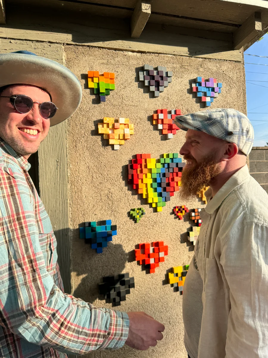 Dave on the left and Benny on the right beside a sunlit wall of colorful block hearts at the Art Blocks house in Marfa.