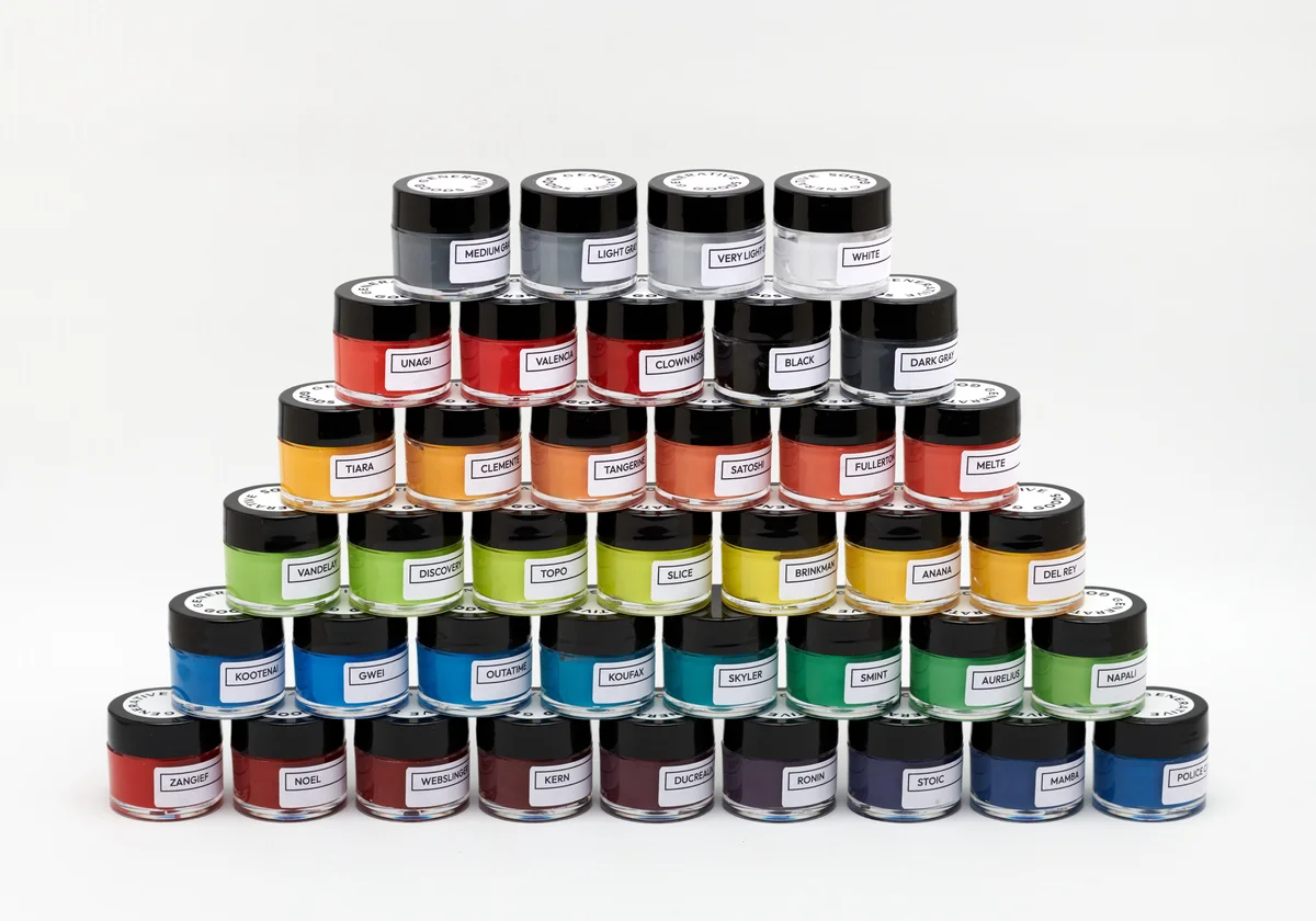 A pyramid of small Generative Goods paint jars with labeled colors, from reds and yellows through greens, blues, and grays.