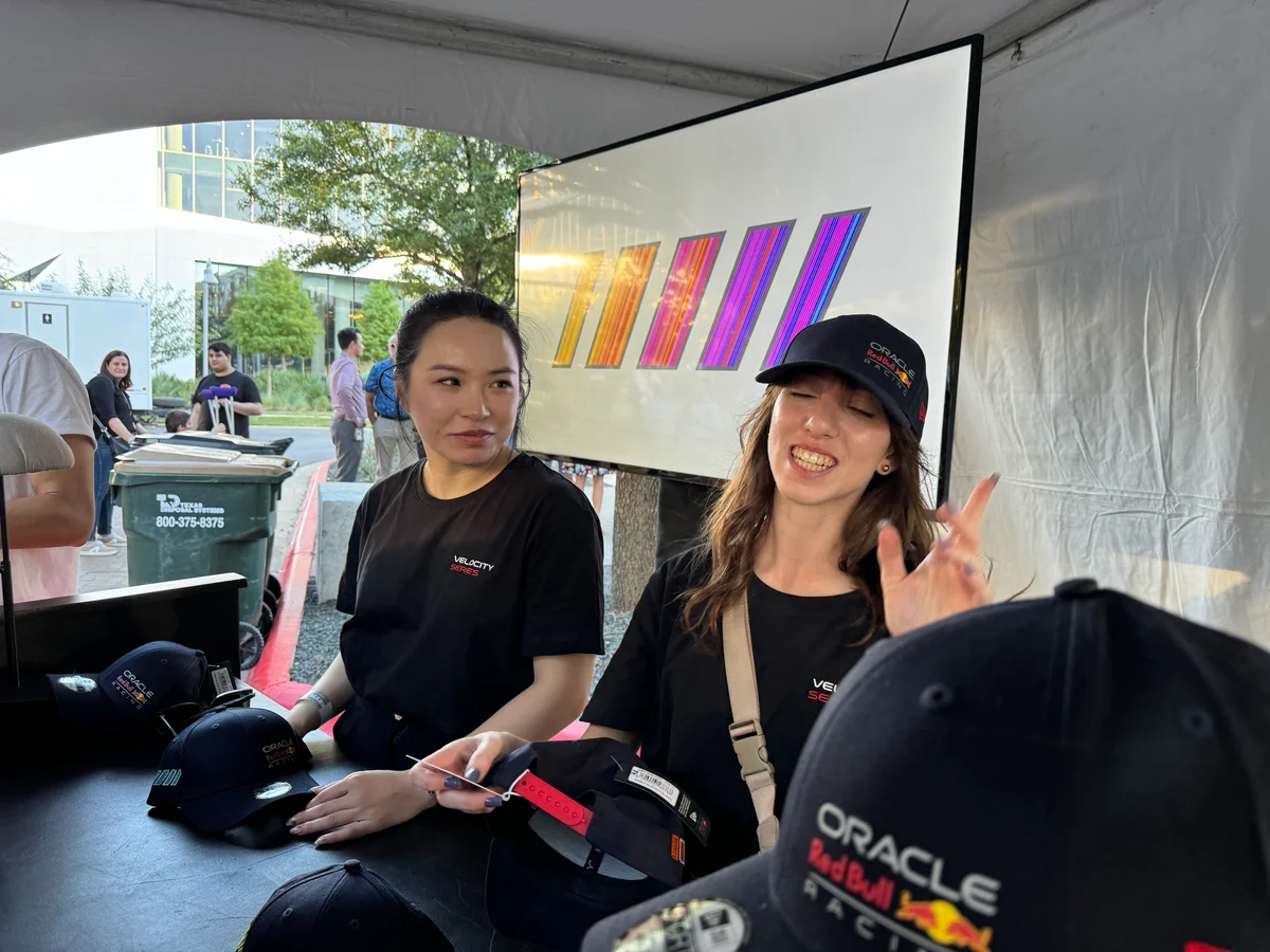 Two people behind the activation counter holding caps, with an embroidered cap on display and a large digital slash composition behind them.