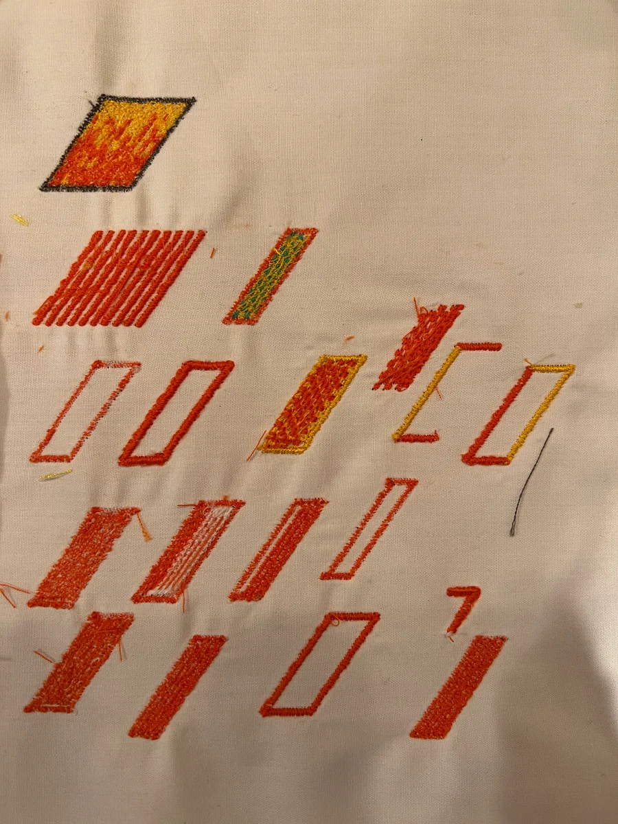 A pale fabric swatch covered with embroidered slash tests in orange and yellow, including empty outlines, filled shapes, and loose threads.