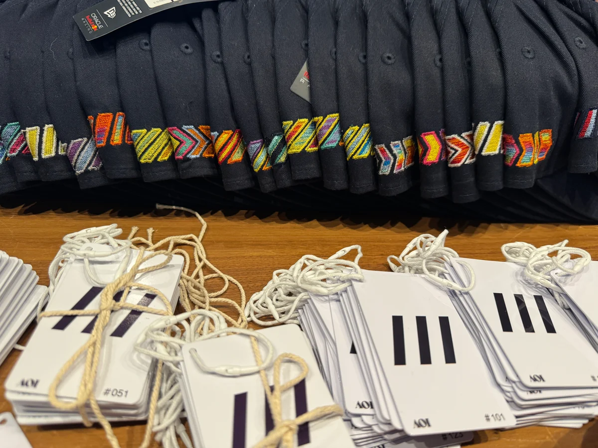 Rows of dark caps embroidered with different slash and chevron compositions, alongside stacks of numbered white cards with cords.