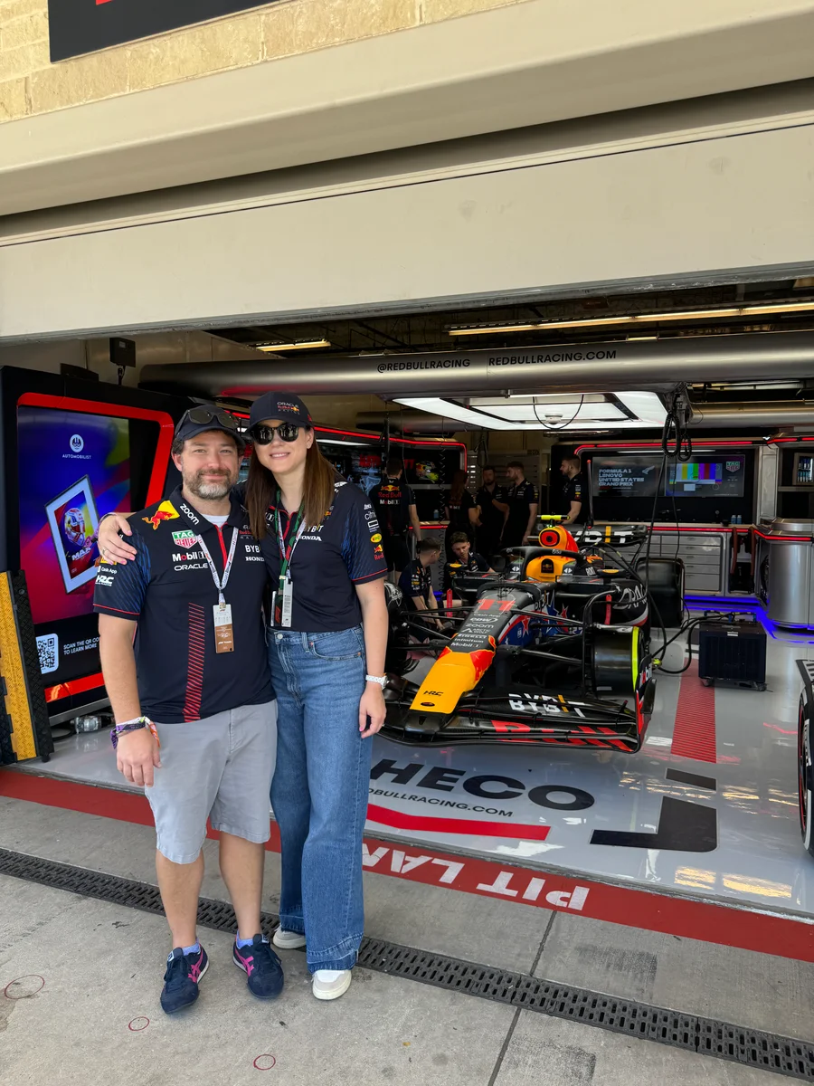 Erick and Mara standing together at the entrance to the Red Bull Racing garage, with a Formula 1 car behind them.