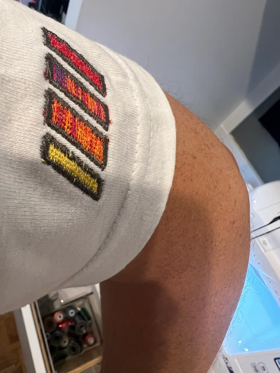 Four embroidered slashes in warm colors with dark borders on the sleeve of a white shirt being worn.