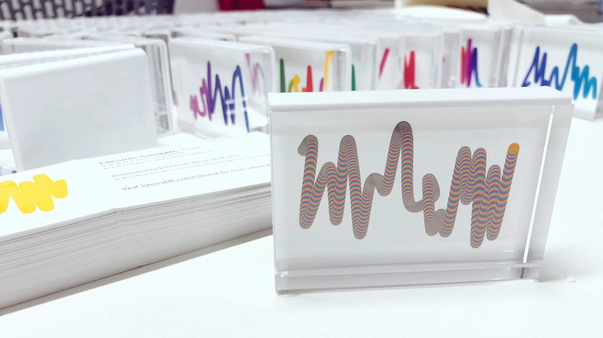 An early rainbow Squiggle print in a clear frame beside a stack of printed cards, with more framed prints behind it.