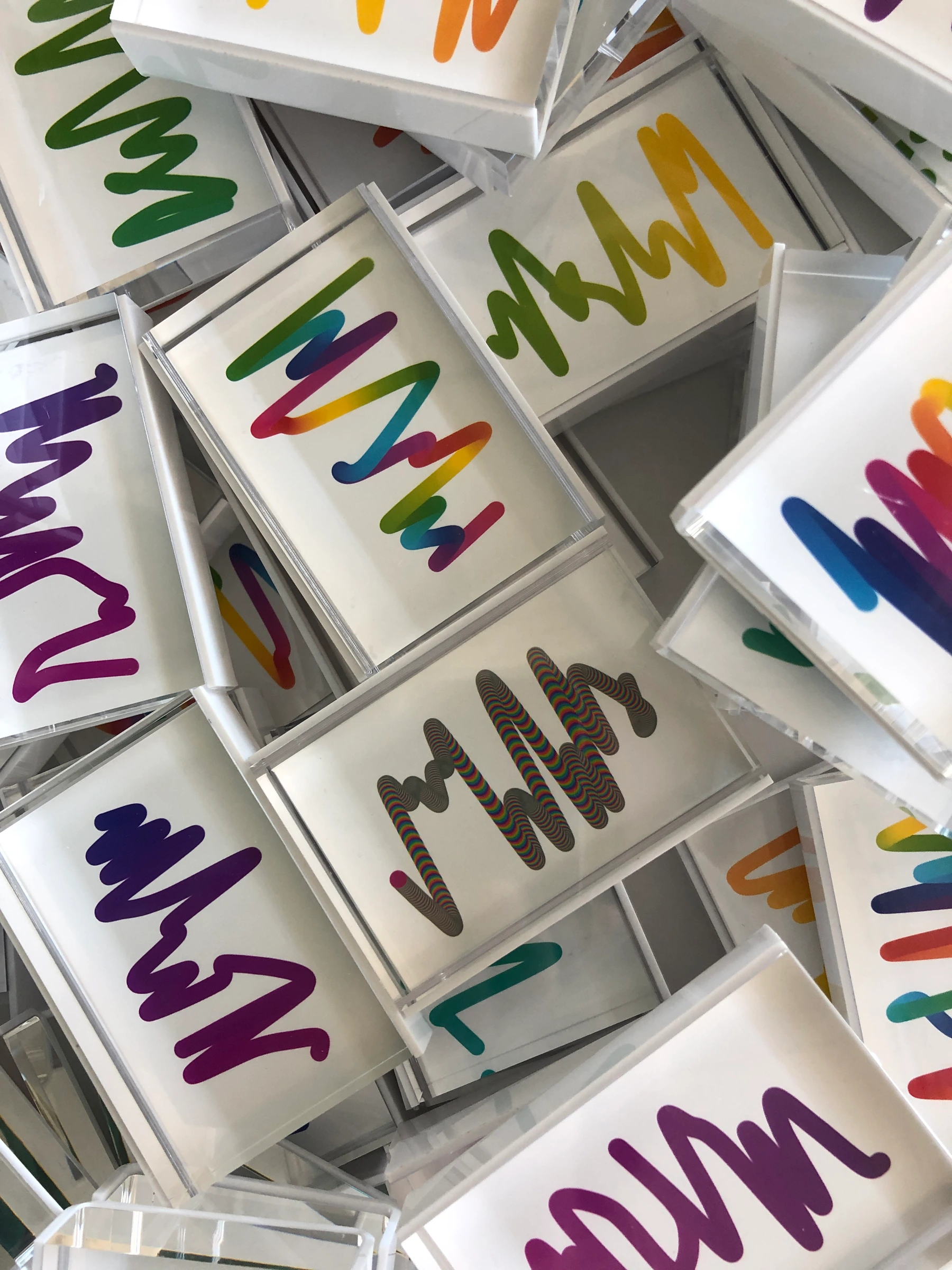 An overhead photograph of overlapping early Squiggle prints in clear frames, showing a variety of shapes and colors.